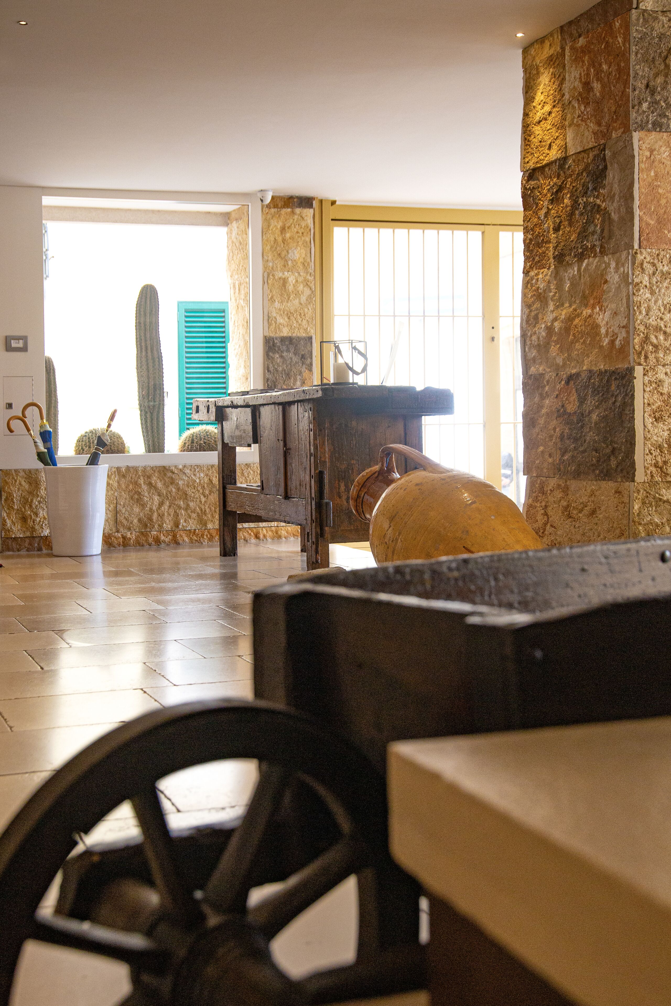 Una habitación con pared de piedra, un banco de madera y un cactus en la esquina.