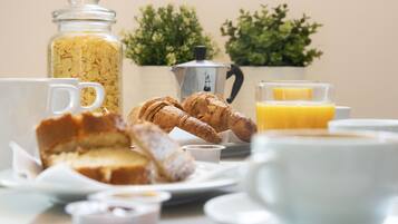 Une table mise pour le petit-déjeuner avec une cafetière, des croissants, un verre de jus d’orange et un bocal de céréales.