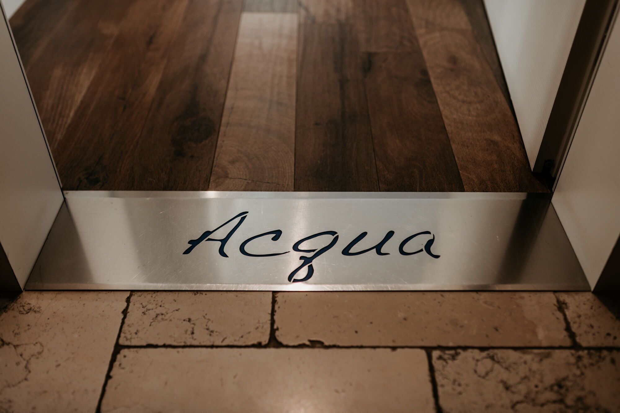 Un letrero de metal con la palabra "Acqua" sobre un piso de madera.