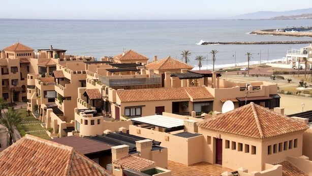 Um hotel costeiro com vários edifícios, com telhados de terracota e fachadas bege, com vista para o mar.