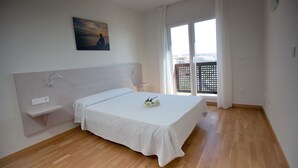 Quarto com cama, mesa de cabeceira, prateleira na parede, quadro e vista pela janela.