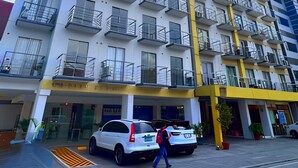 A multi-story hotel with balconies, a parking area, and a pedestrian walkway. - Dian SUITES 1 (Makati)
