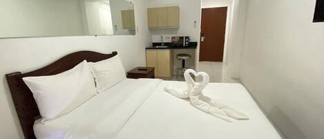 A hotel room with a bed, a wooden headboard, a white bedspread, and a heart-shaped towel arrangement.