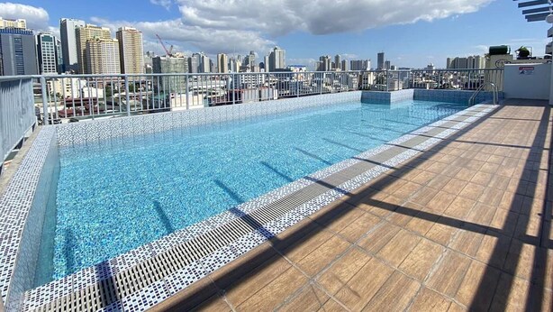 A rooftop pool with a city skyline view, surrounded by a metal railing and a wooden deck. - Dian SUITES 1 (Makati)