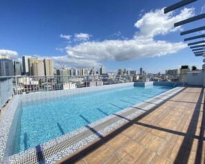 A rooftop pool with a city skyline view, surrounded by a metal railing and a wooden deck.