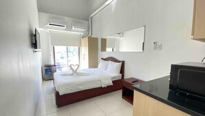 A hotel room with a bed, a desk with a microwave, a TV, and a bathroom with a shower and toilet. - Dian SUITES 1 (Makati)