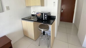 A compact kitchen with a microwave, a sink, and a stool. - Dian SUITES 1 (Makati)