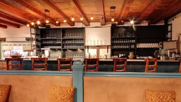 A bar area with wooden chairs and a counter, shelves with glasses and bottles, and a rustic ceiling.