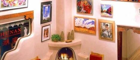 A cozy lounge area with a fireplace, red sofas, and a variety of framed artworks on the walls.