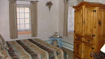 Une chambre à coucher avec un lit, une armoire en bois, une petite table avec quelques objets et des rideaux aux fenêtres.