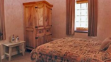 A bedroom with a large wooden wardrobe, a small bedside table with bottles, and a patterned bedspread.