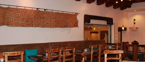 A restaurant interior with wooden furniture, a patterned wall hanging, and an exit sign.