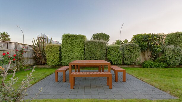 A wooden picnic table with benches in a garden area with a paved walkway. - Bella Vista Motel Hamilton (Hamilton)