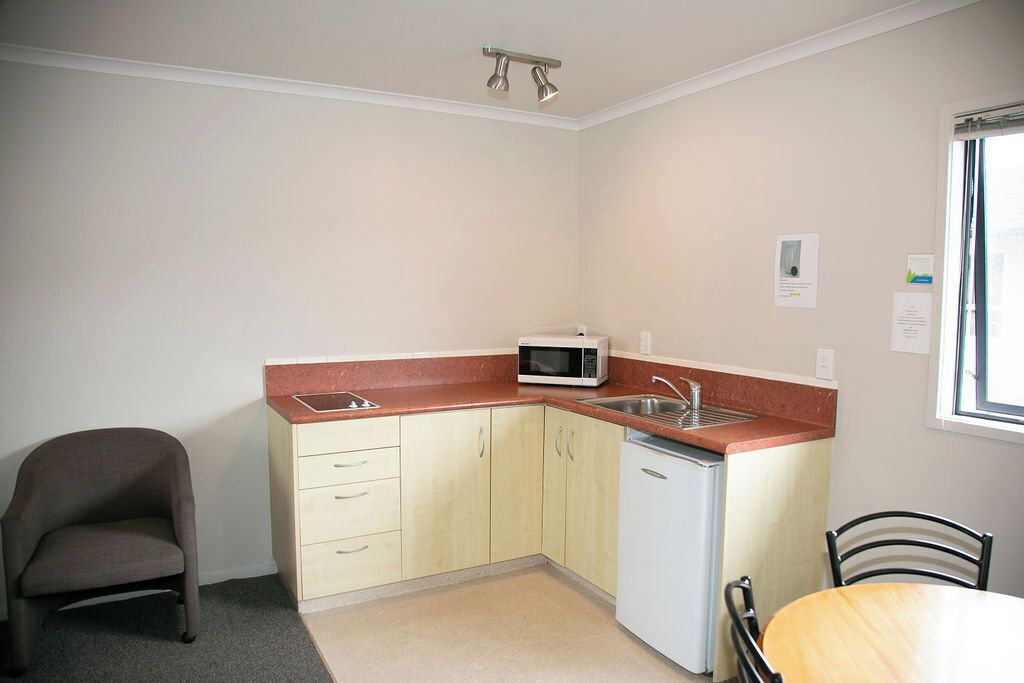 A compact kitchen with a microwave, sink, and a small refrigerator. There is a chair and a table, suggesting a dining area.