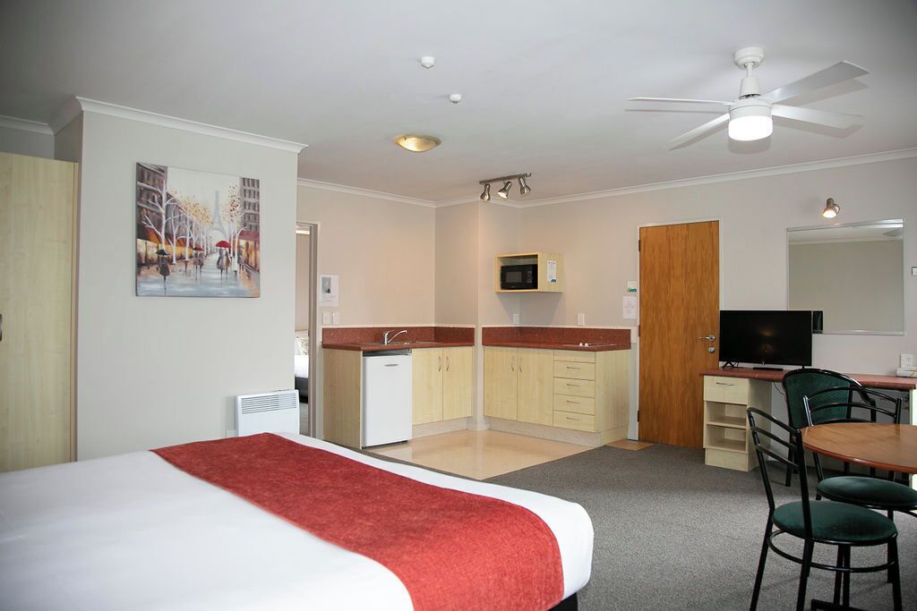 Quarto de hotel com cama, cozinha compacta, área de refeições e televisão.