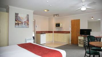 Quarto de hotel com cama, cozinha compacta, área de refeições e televisão.
