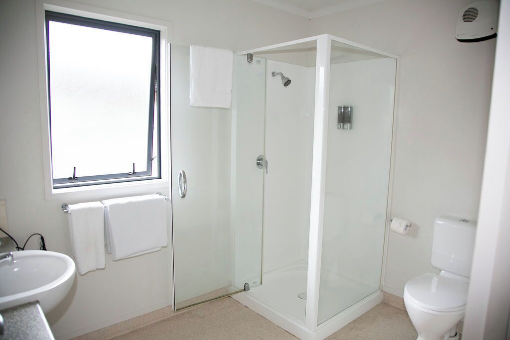A bathroom with a glass-enclosed shower, a toilet, a sink, and a window.