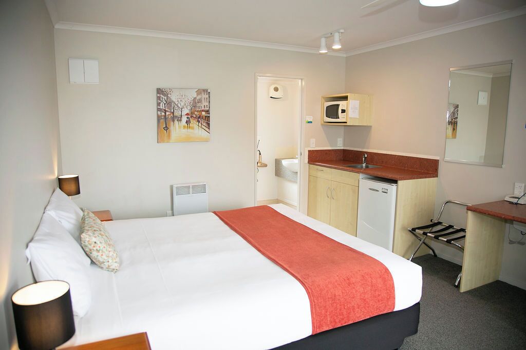 A hotel room with a bed, a desk with a microwave, a small kitchenette, and a bathroom.