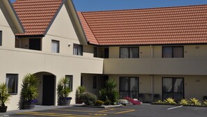 A hotel with a red-tiled roof, multiple balconies, and a parking lot with marked spaces. - Bella Vista Motel Hamilton (Hamilton)