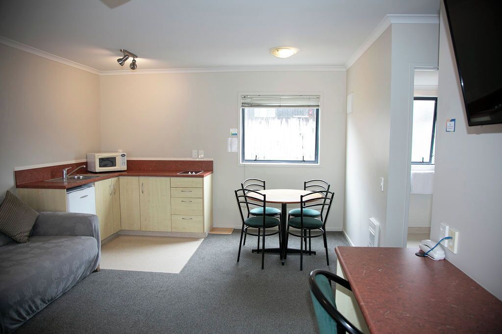 A compact living space with a kitchenette, a dining area with four chairs, a sofa, and a television mounted on the wall.