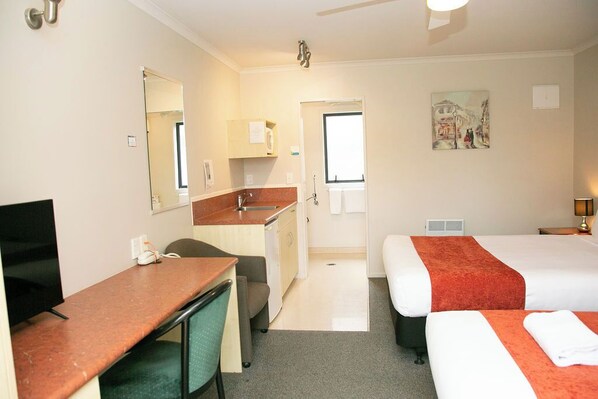 A hotel room with a desk, two beds, a small kitchenette, and a painting on the wall. - Bella Vista Motel Hamilton (Hamilton)