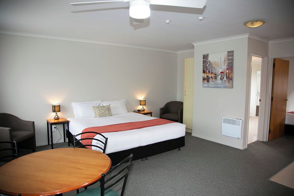 A hotel room with a bed, bedside tables, a chair, a table, and a painting on the wall.