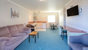 A compact living space with a sofa, a small table, a kitchenette, and a TV mounted on the wall. - Bella Vista Motel Hamilton (Hamilton)