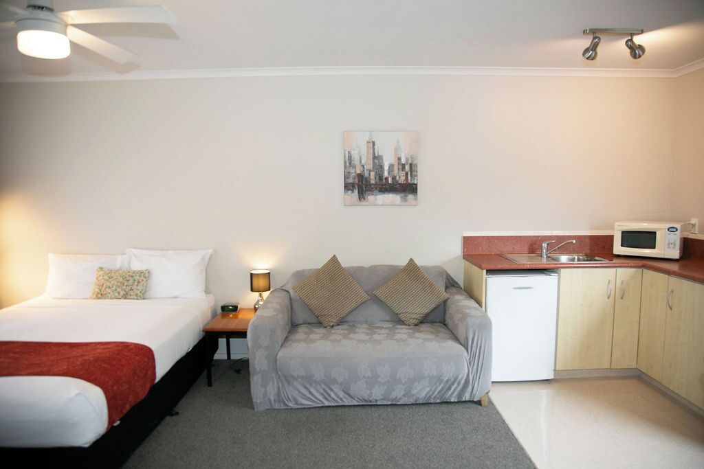 Una habitación de hotel pequeña con cama, sofá, una mesita con lámpara, microondas y lavamanos.