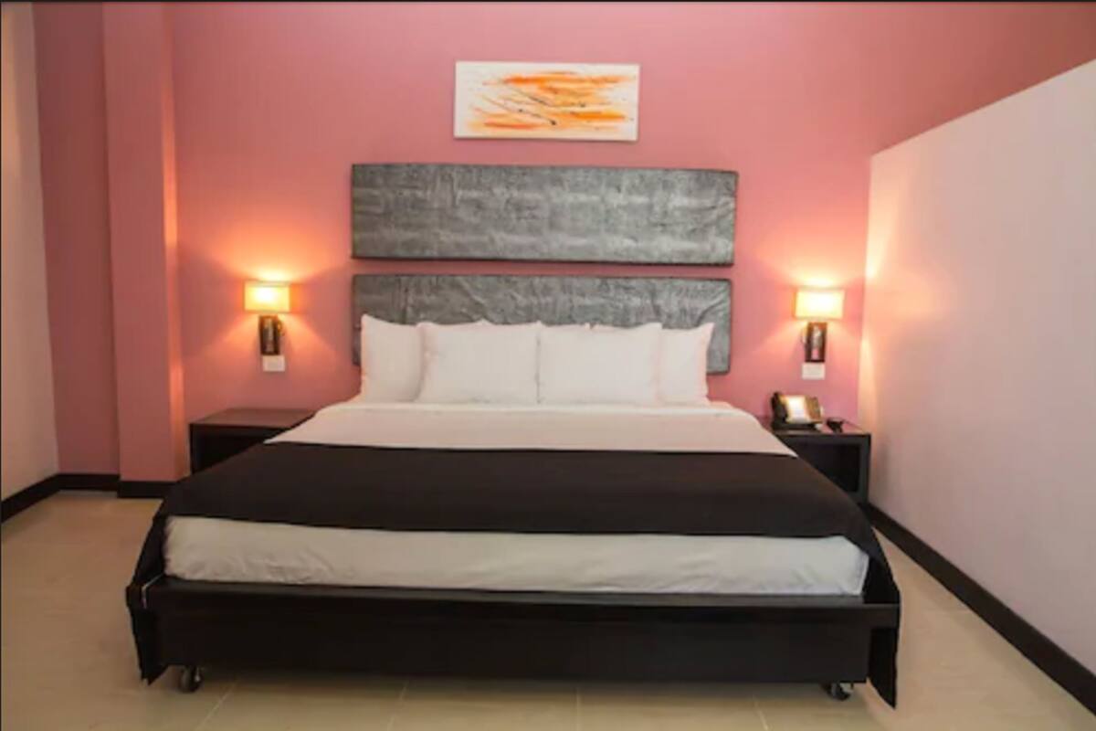 A large bed with a headboard, two bedside tables, and wall-mounted lamps.