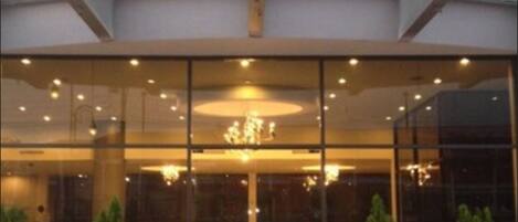A modern building with a glass facade, a central circular light fixture, and potted plants at the entrance.