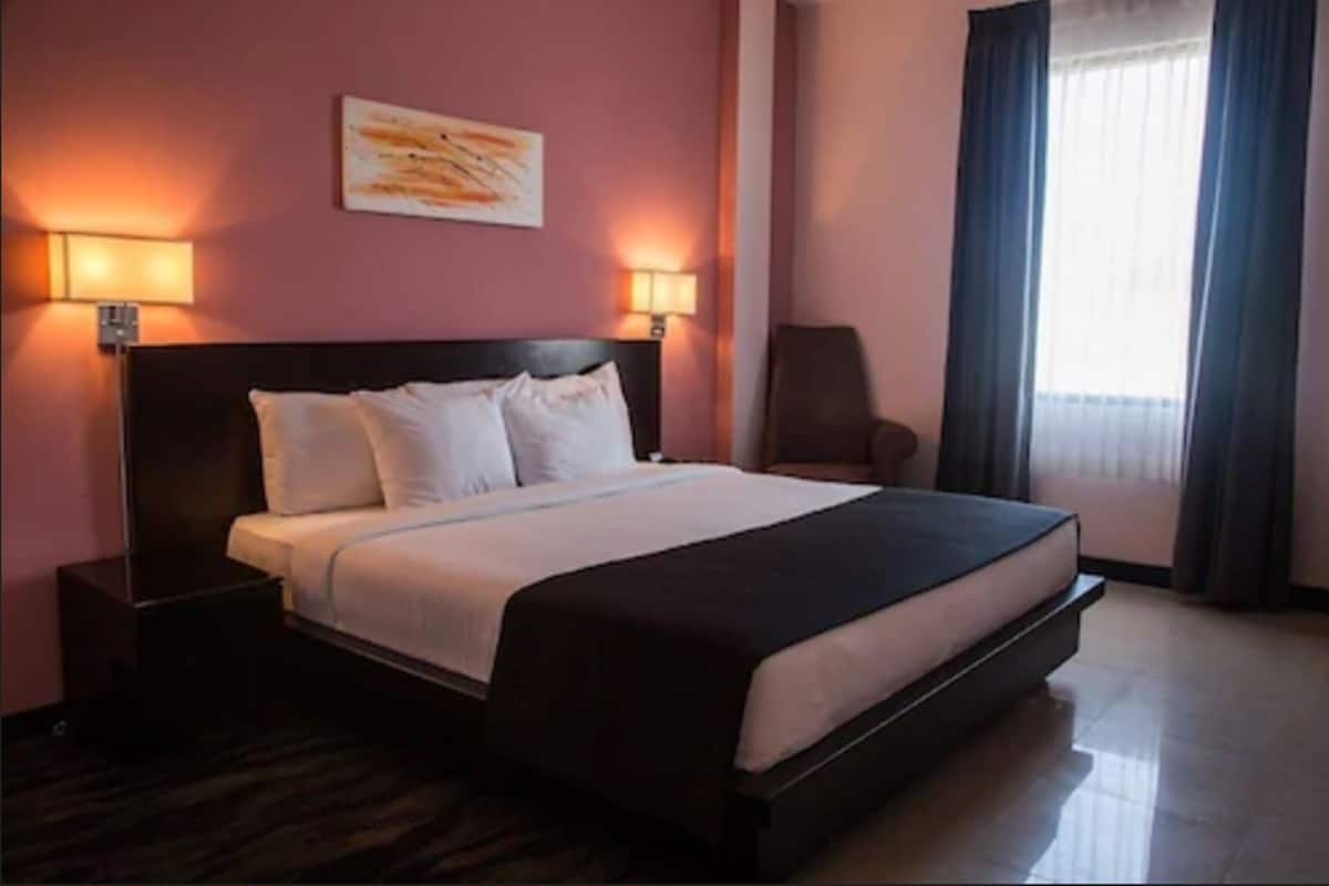 A hotel room with a large bed, two bedside tables, a chair, and a window with curtains.