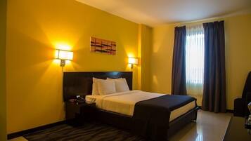 A hotel room with a large bed, two bedside lamps, a headboard, a nightstand, a desk, and a chair.