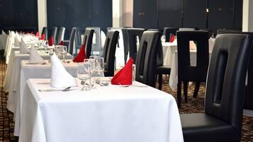 Comedor con mesas dispuestas para el servicio, cada una con mantel blanco, servilletas rojas y cubiertos.