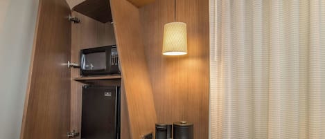 A compact kitchenette with a microwave, mini-fridge, and coffee maker, featuring wooden cabinetry and a hanging pendant light.