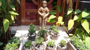 A statue of a figure in traditional attire, surrounded by potted plants in a courtyard with a wooden door in the background. - Thyda Villa (Siem Reap)
