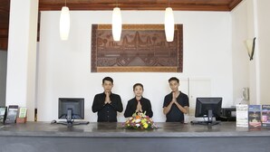 A reception desk with three individuals standing behind it, a floral arrangement on the counter, and a large wall mural above. - Thyda Villa (Siem Reap)