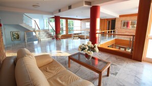 Un vestíbulo amplio con un sofá color beige, una mesa de centro de vidrio con flores, una escalera y vistas al exterior.