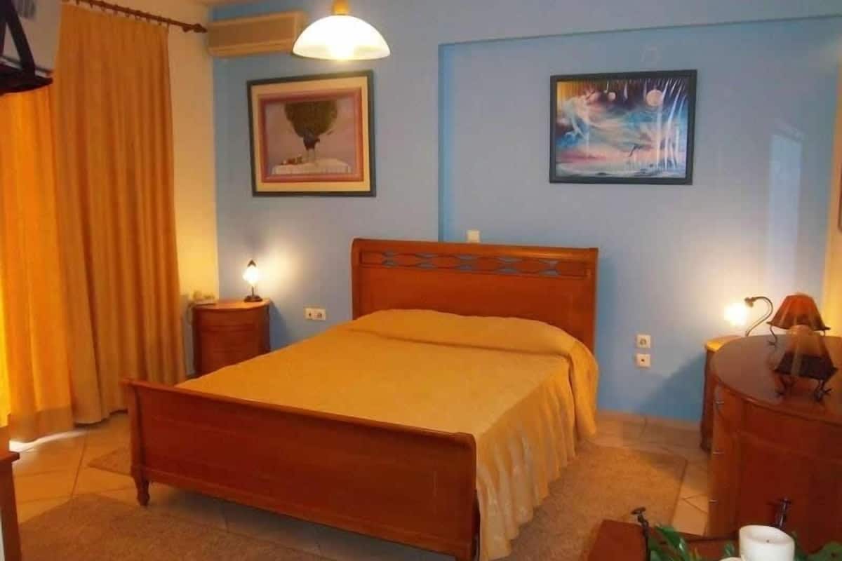 Une chambre à coucher avec un lit en bois, deux tables de chevet avec des lampes, une commode et deux tableaux encadrés accrochés au mur.