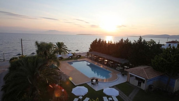 Una piscina con sillas de descanso y sombrillas, rodeada de vegetación y con vistas al mar.