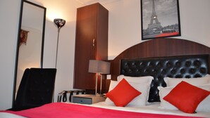 Een hotelkamer met een groot bed, een kledingkast, een bureau, een stoel, een lamp en een lijst met een afbeelding van de Eiffeltoren.