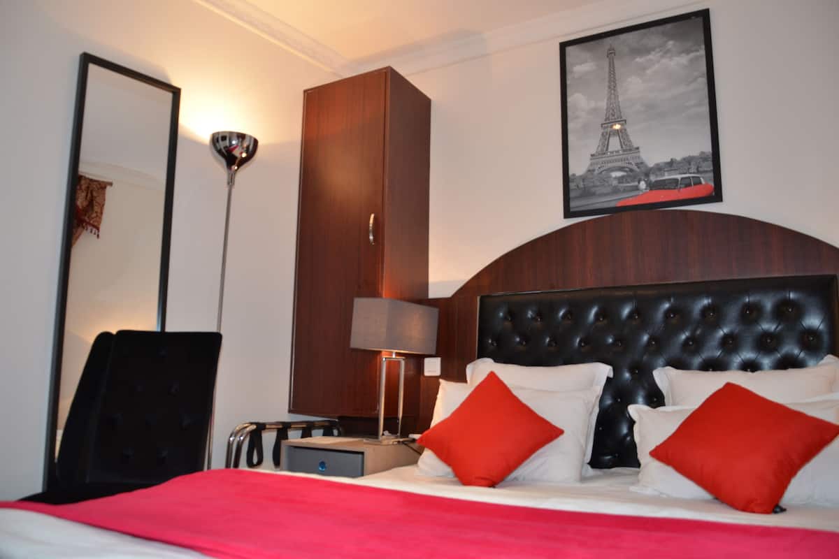 A hotel room with a large bed, a wardrobe, a desk, a chair, a lamp, and a framed picture of the Eiffel Tower.