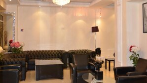 Een ruime lobby met een grote, gestoffeerde bank, verschillende fauteuils en een salontafel. Er hangen twee grote kroonluchters en een spiegel aan de muur.