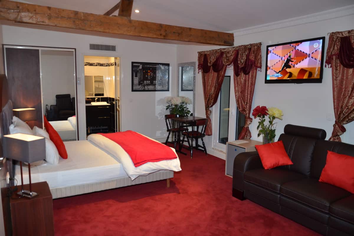 A hotel room with a bed, a sofa, a TV, a dining table, and a chair.