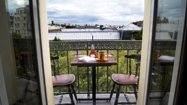 Een balkon met een tafel, twee stoelen, een fles en een beker.