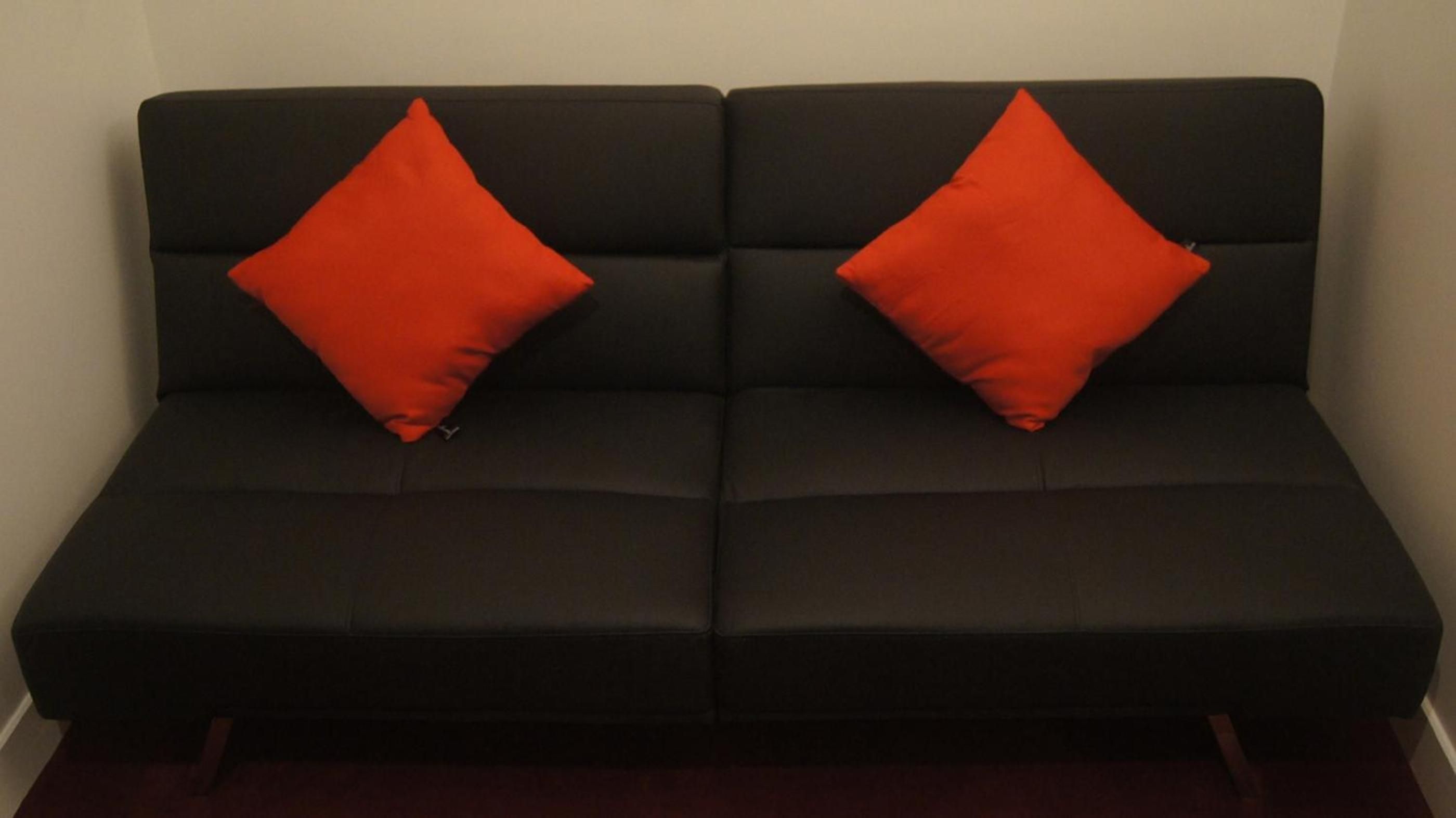 Un sofá negro con dos almohadas rojas.