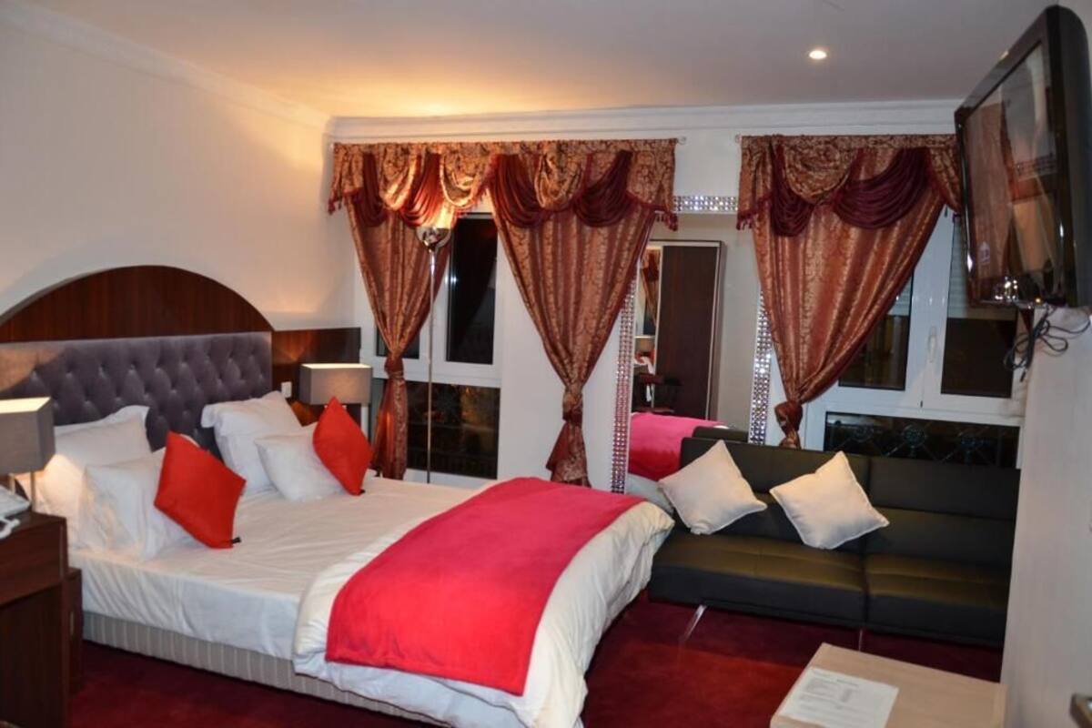 A hotel room with a large bed, a sofa, a TV, and curtains.