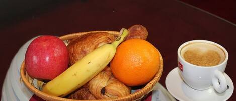 A basket with a red apple, a banana, and an orange on a table next to a cup of coffee.