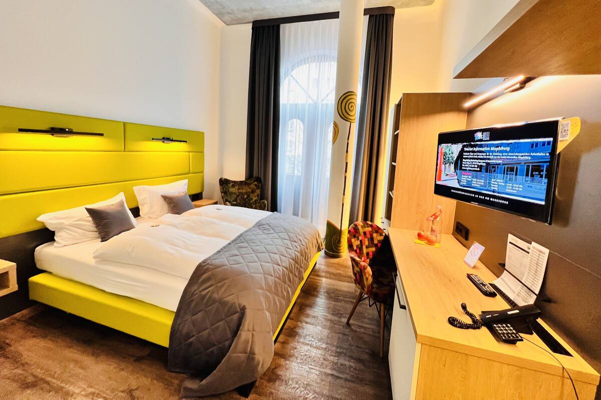 A hotel room with a bed, a desk with a computer, a phone, and a TV.