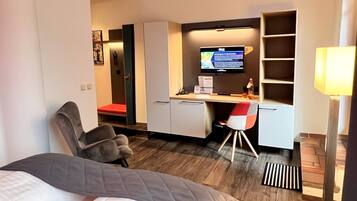 Habitación de hotel con cama, escritorio, computadora, silla, televisor y lámpara.