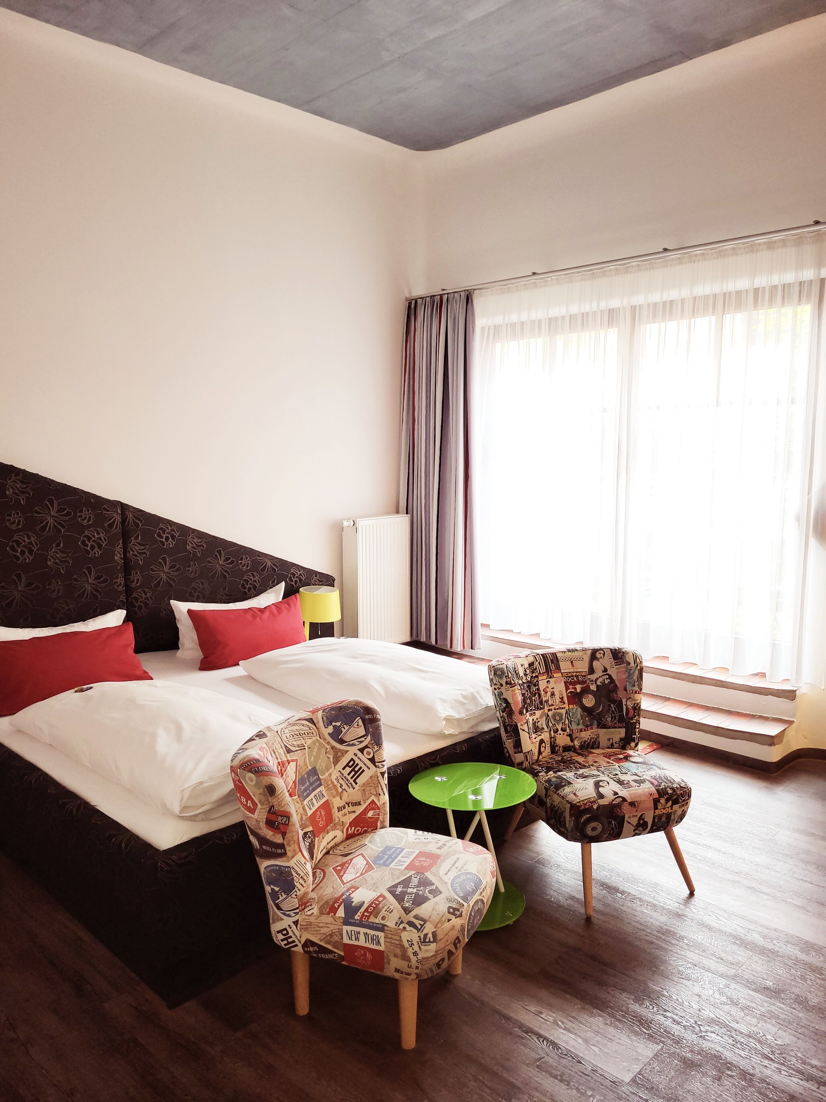 A hotel room with a large bed, two chairs, a small table, and a window with curtains.